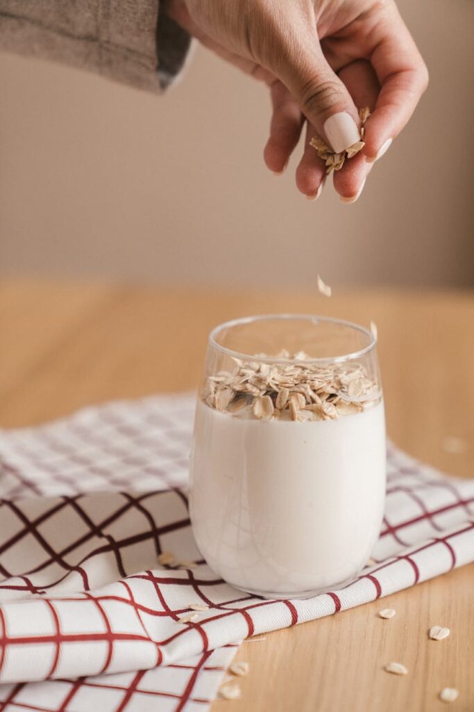 person sprinkling oats in a glass of smoothie