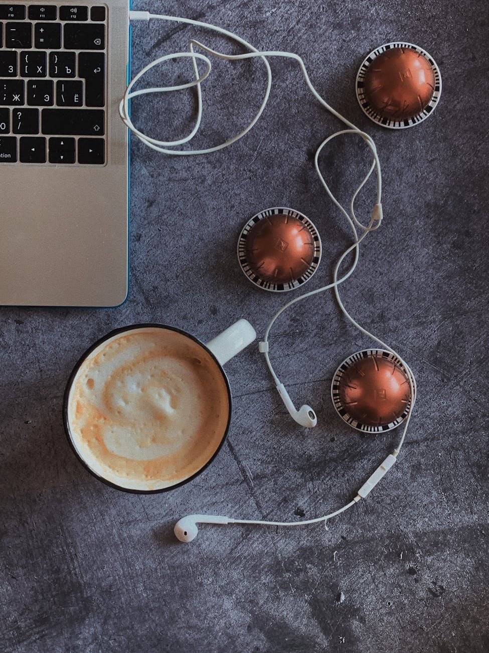 headphones connected with laptop placed near cappuccino