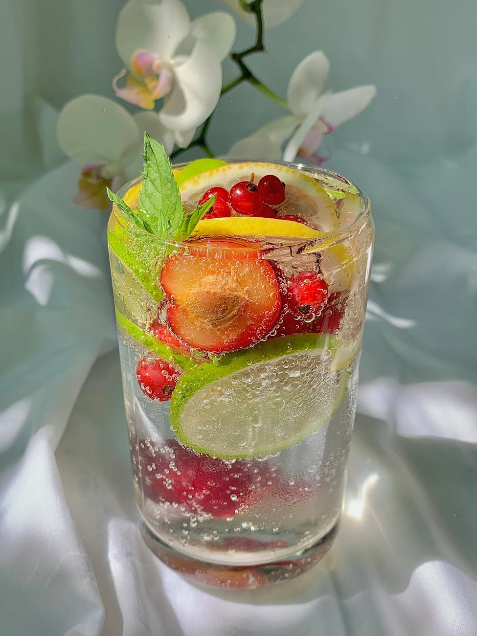 a glass of bubbly citrus drink with red berries and mint leaves